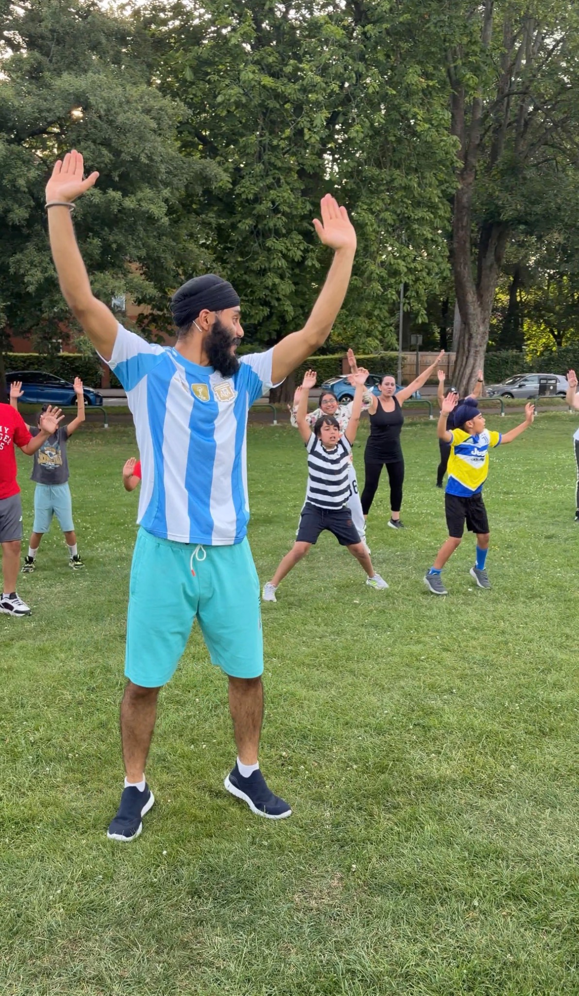 An instructor leading an outdoor Bhangra workshop for adults and children