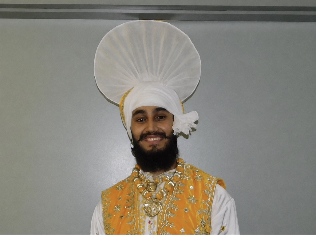 A smiling LU Bhangra dancer in a yellow and white traditional costume